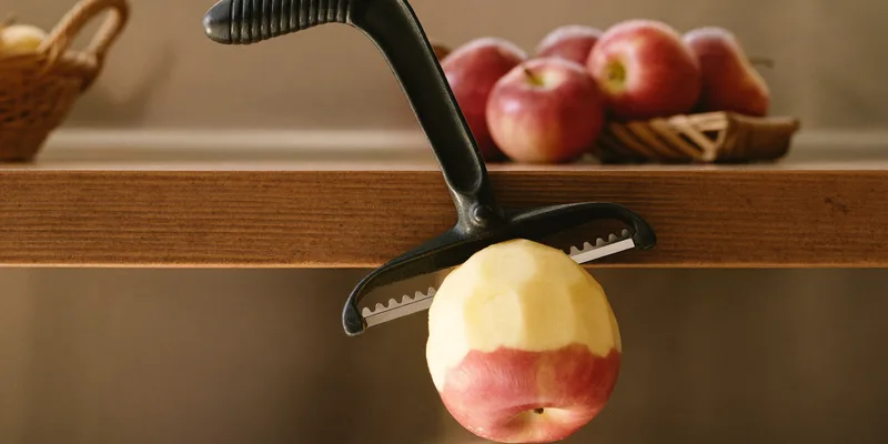 Hand crank apple peeler clamped to the table with a peeled apple