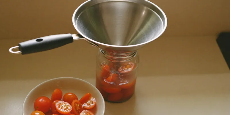 Stainless wide mouth funnel in a jar being filled with diced tomatoes