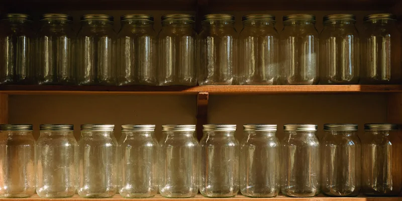 Rows of empty plain glass canning jars on wooden pantry shelves