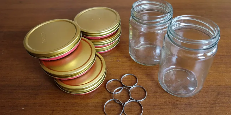 Stack of gold canning lid discs and screw bands beside empty jars