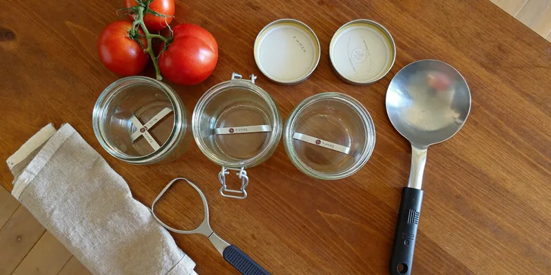 Flat lay of canning jars, lids, ladle, jar lifter and fresh tomatoes