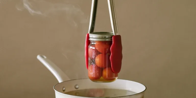 Canning tongs holding a jar of tomatoes over a steaming pot