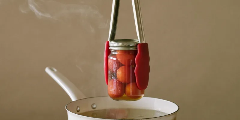 Canning tongs holding a jar of tomatoes over a steaming pot