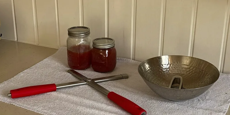 Jar lifter, jam jars and a metal bowl on a linen towel