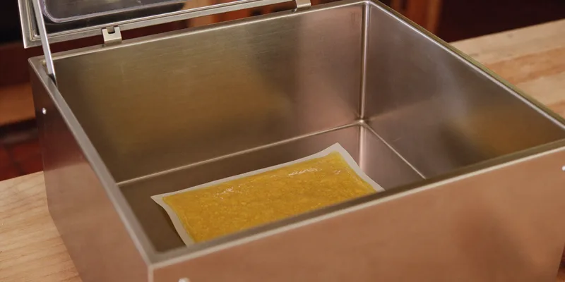 Open stainless vacuum chamber with a bag of soup inside