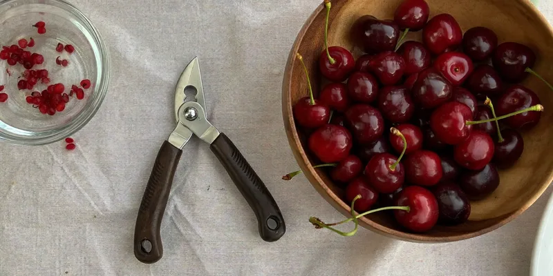Cherry pitting tool beside a bowl of dark cherries