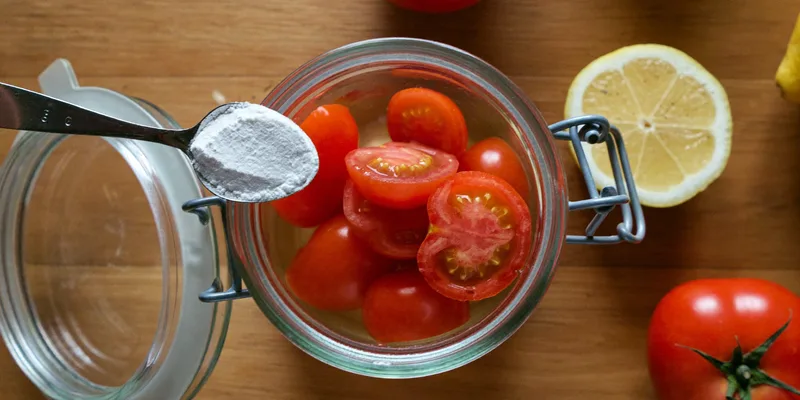 Spoon of white powder resting on a jar packed with tomato halves