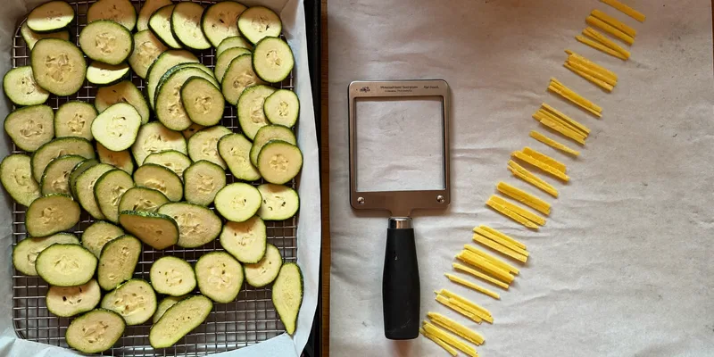 Thick uneven zucchini slices beside a mandoline with even slices