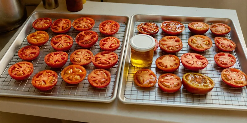 Halved tomatoes on racks beside a jar of oil
