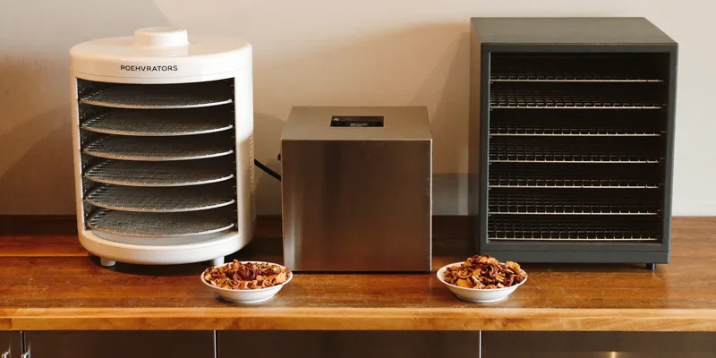 Three different dehydrators in a row with bowls of dried fruit
