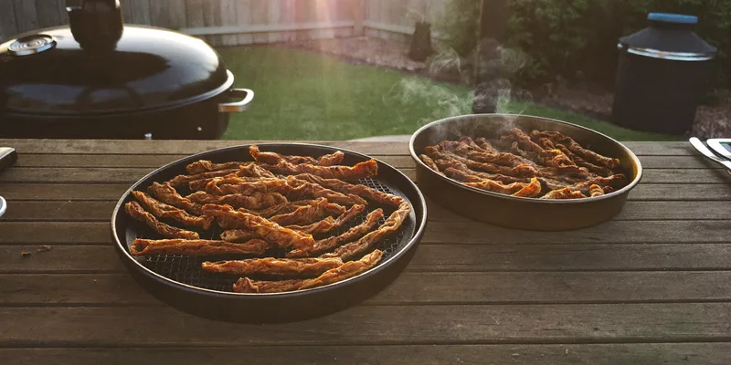 Jerky on a dehydrator tray and on a smoker grate outdoors
