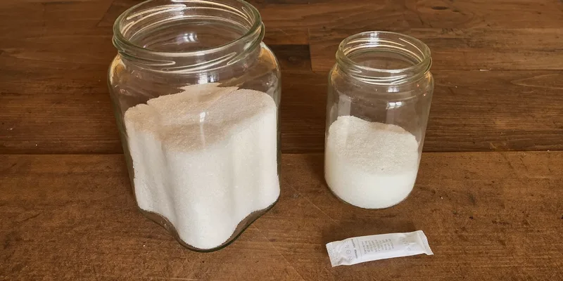 Jar of clumped hard sugar beside loose sugar and a sachet