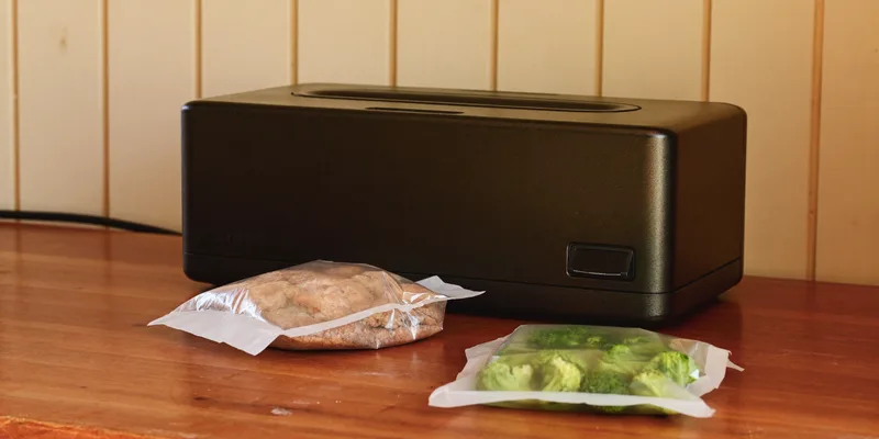 Compact black vacuum sealer with sealed bags in front