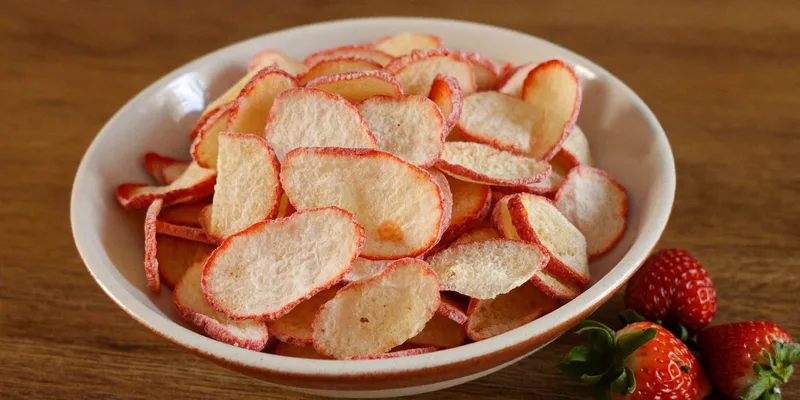 Bowl of crisp freeze dried strawberry slices next to fresh strawberries