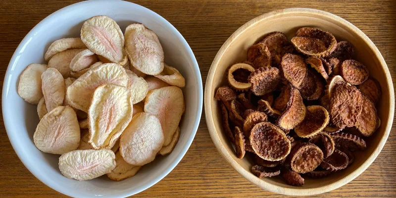 Bowl of pale freeze dried strawberries beside dark dehydrated slices