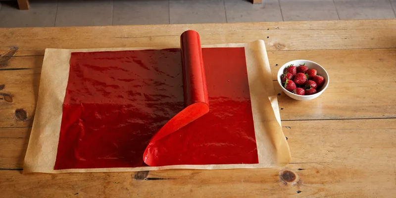 Sheet of red fruit leather partly rolled with fresh strawberries