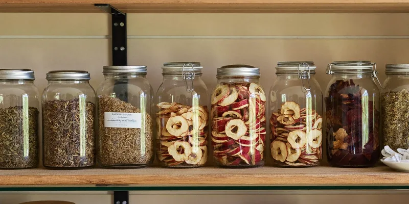 Jars of dried apples, herbs and vegetables on a pantry shelf