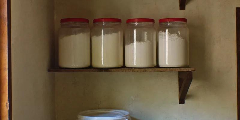 Jars of flour with red lids and a white bucket on a shelf