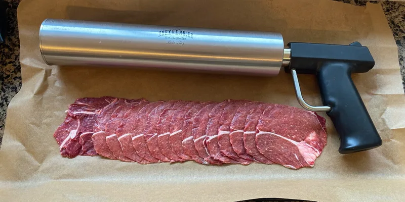 Metal jerky gun beside pressed strips of seasoned ground meat