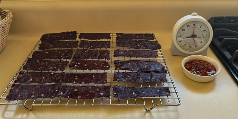 Jerky strips on a wire rack beside an analog kitchen timer