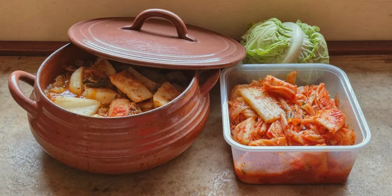 Earthenware onggi pot beside a container of kimchi