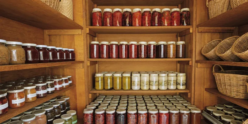 Tidy pantry shelves with rows of preserve jars and baskets
