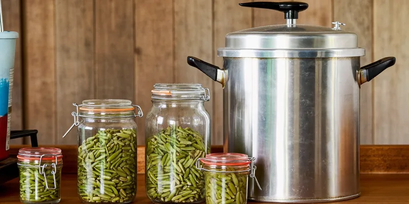 Vintage aluminum pressure canner with clamp lid beside jars of green beans
