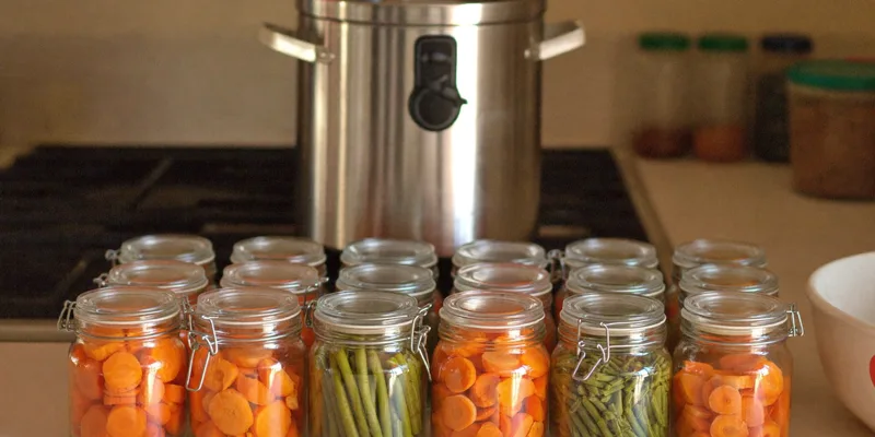 Jars of carrots and green beans in front of a stainless pressure canner on the stove