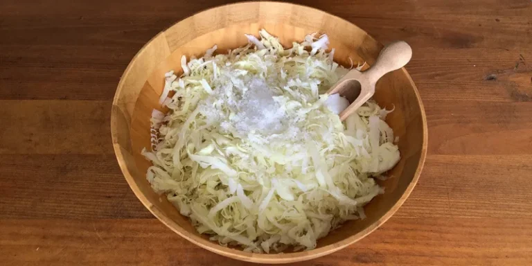 Bowl of shredded cabbage with salt and a wooden scoop