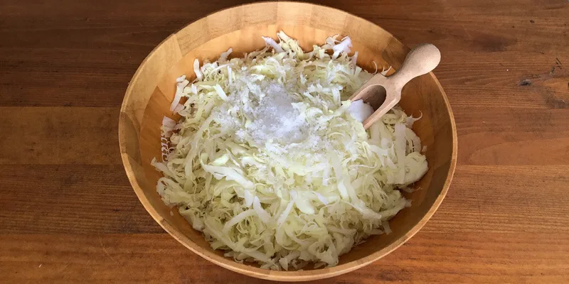 Bowl of shredded cabbage with salt and a wooden scoop