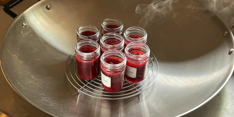 Glass jars of red jam standing on a rack in a wide shallow steam canner pan
