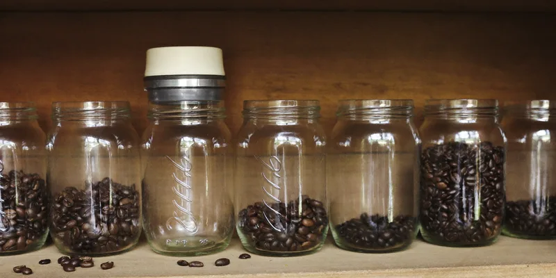 Mason jars of coffee beans with a vacuum jar sealer on a pantry shelf