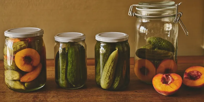 Wide mouth glass jars filled with pickles and peach halves